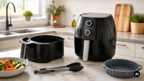 Air fryer genérica com o cesto retirado ao lado, uma forma canelada e uma taça de legumes numa bancada de cozinha.
